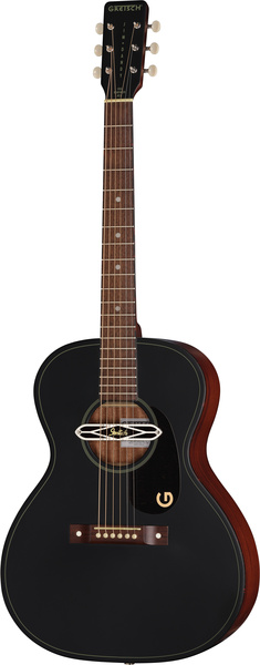 Une guitare folk noire au fini brillant, à six cordes, dotée d'une rosace ronde ornée d'un cache métallique décoratif et portant la lettre G sur le bas du corps. La guitare est équipée de chevilles d'accordage blanches et d'un chevalet en bois.